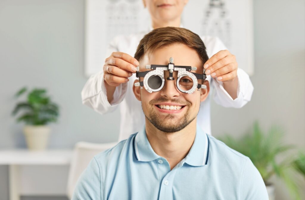 An eye doctor in the background gently places trail vision lenses on their patient during their routine eye exam.