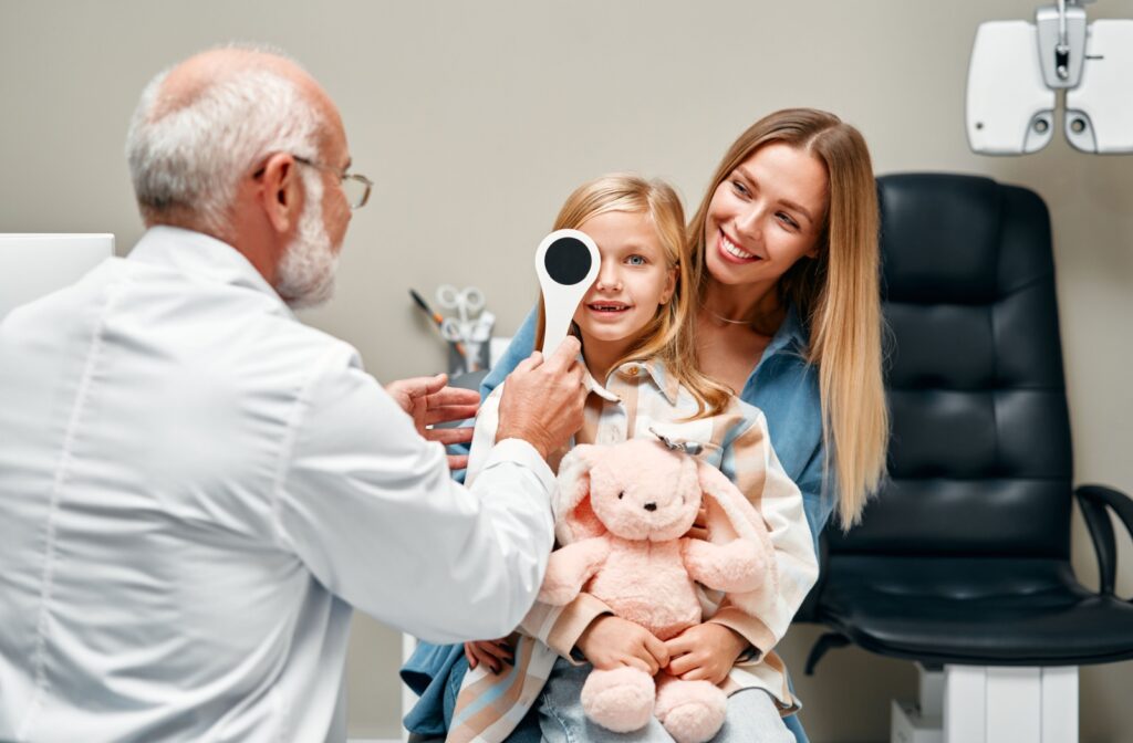 An eye doctor covers a young child's eye to assess their vision during their routine eye exam.
