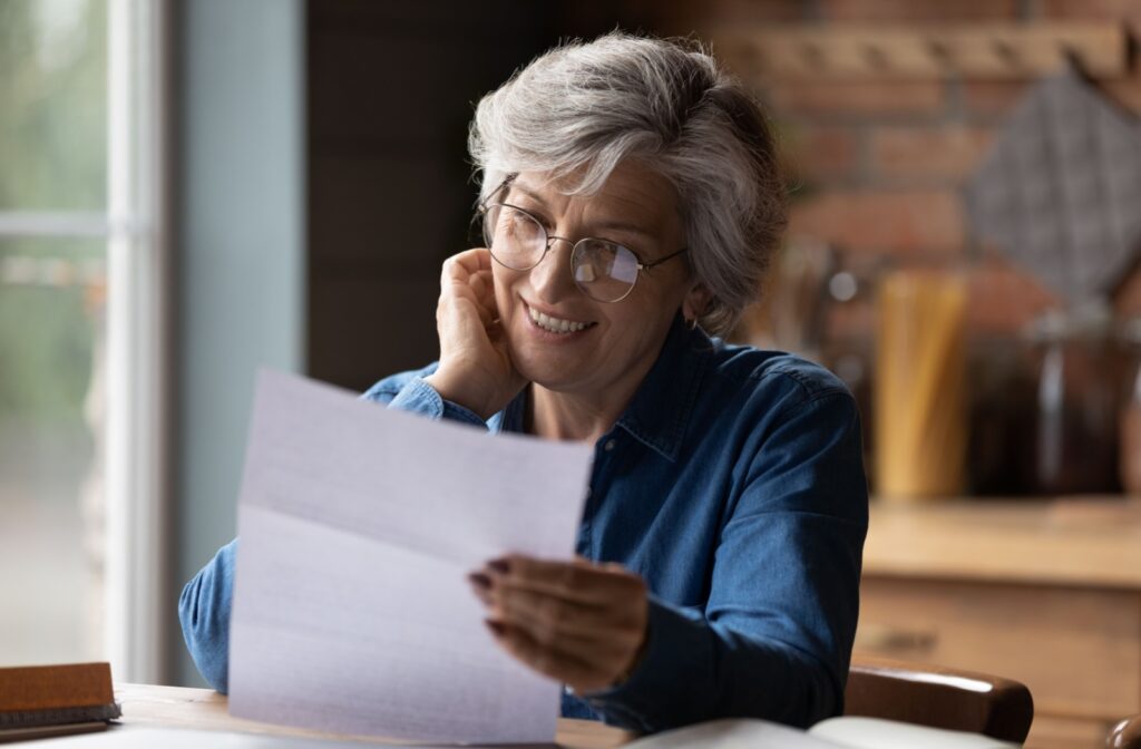 A smiling older adult reading paperwork without strain due to their new reading glasses.
