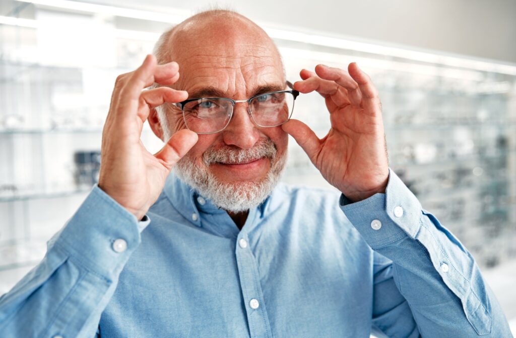An older adult smiling after their eye exam while adjusting their new pair of reading glasses.