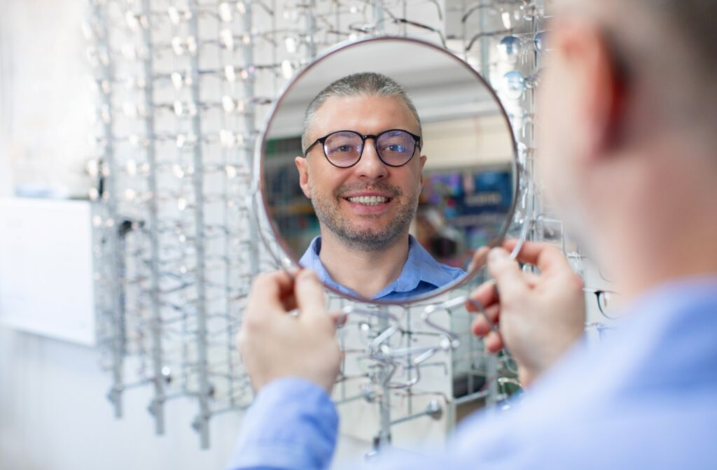 Man smiling while trying on new glasses in front of a mirror.