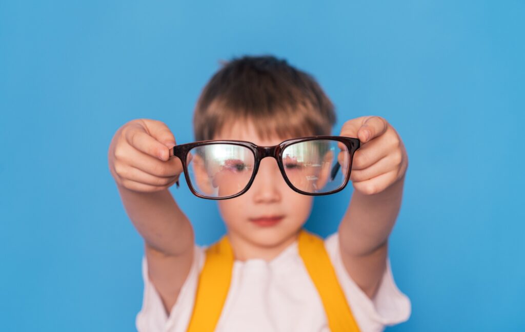A young child with myopia holds a pair of corrective eyeglasses out in front of them.