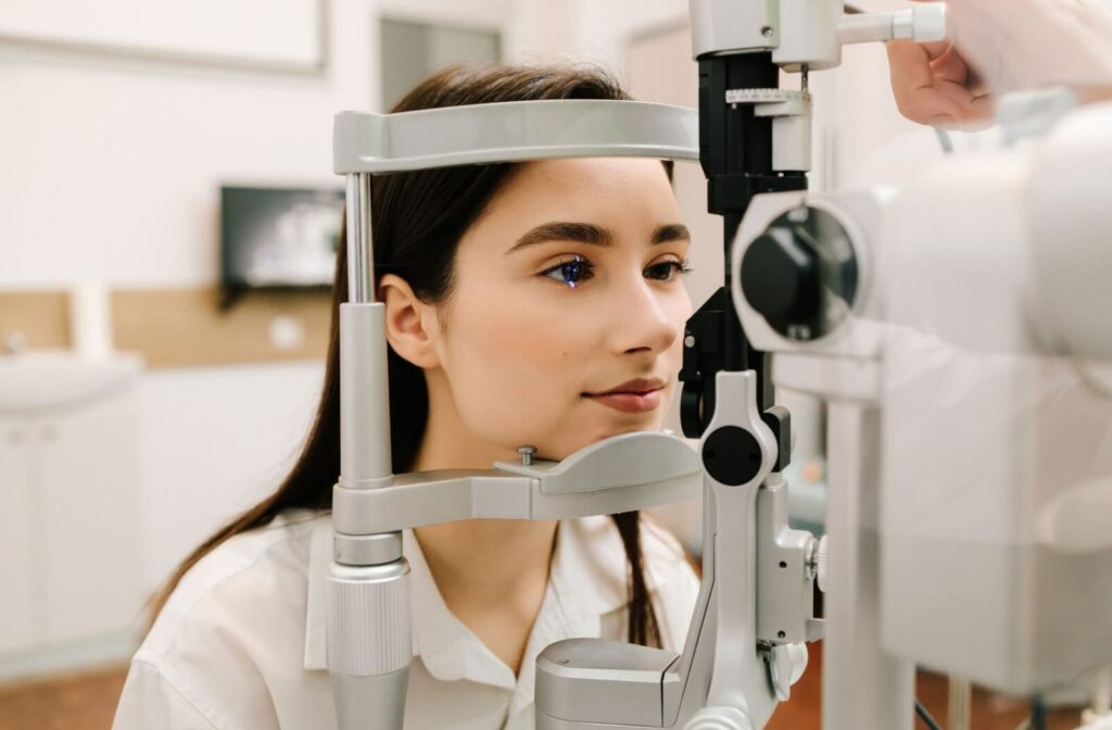 Young woman undergoing an eye exam with a slit lamp machine, illuminated by a blue light during an optometry appointment.