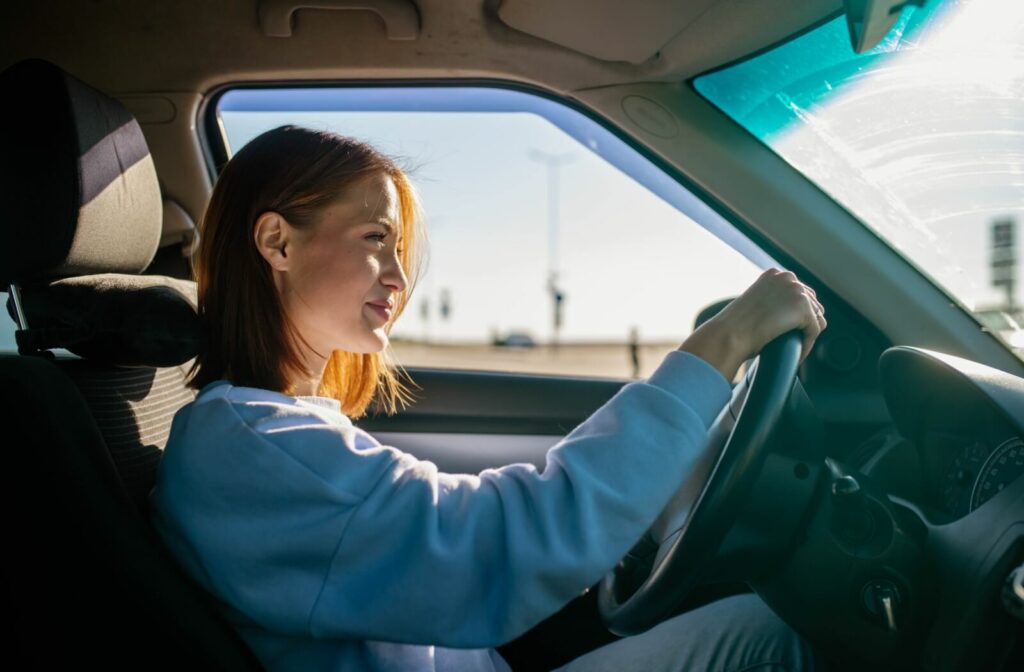 Young woman driving a car on a sunny day, looking ahead with focus and confidence, sunlight streaming through the windshield.