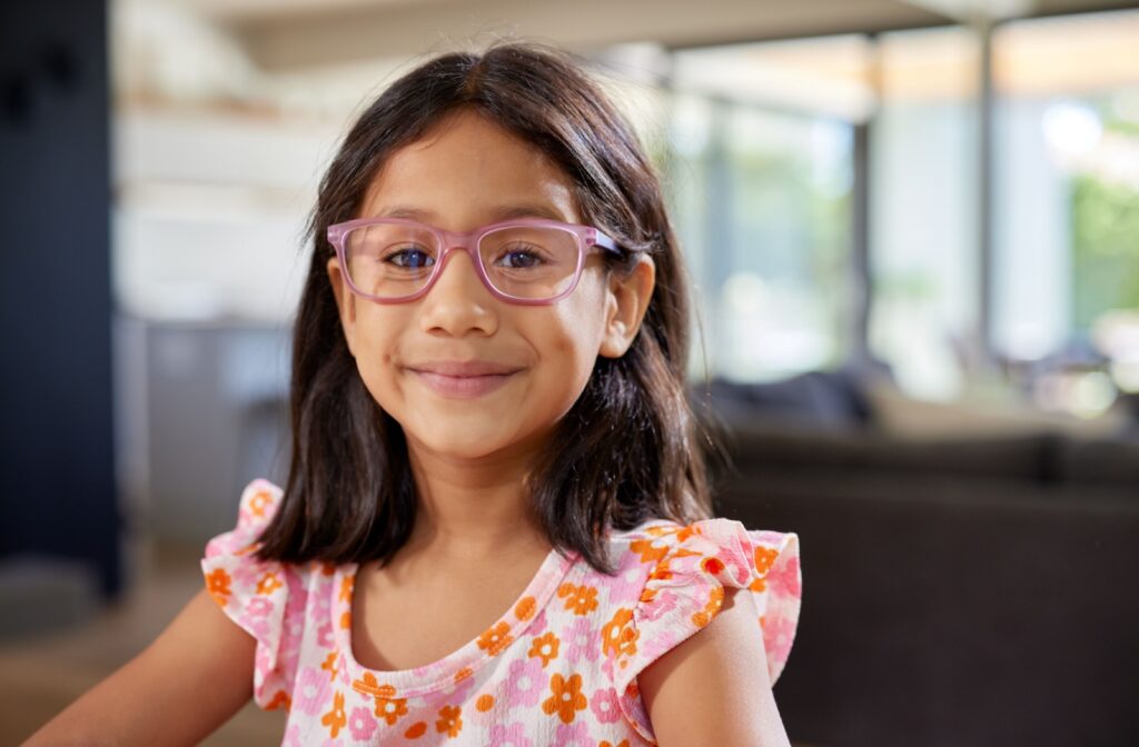 A young girl smiles while wearing a pair of pink glasses