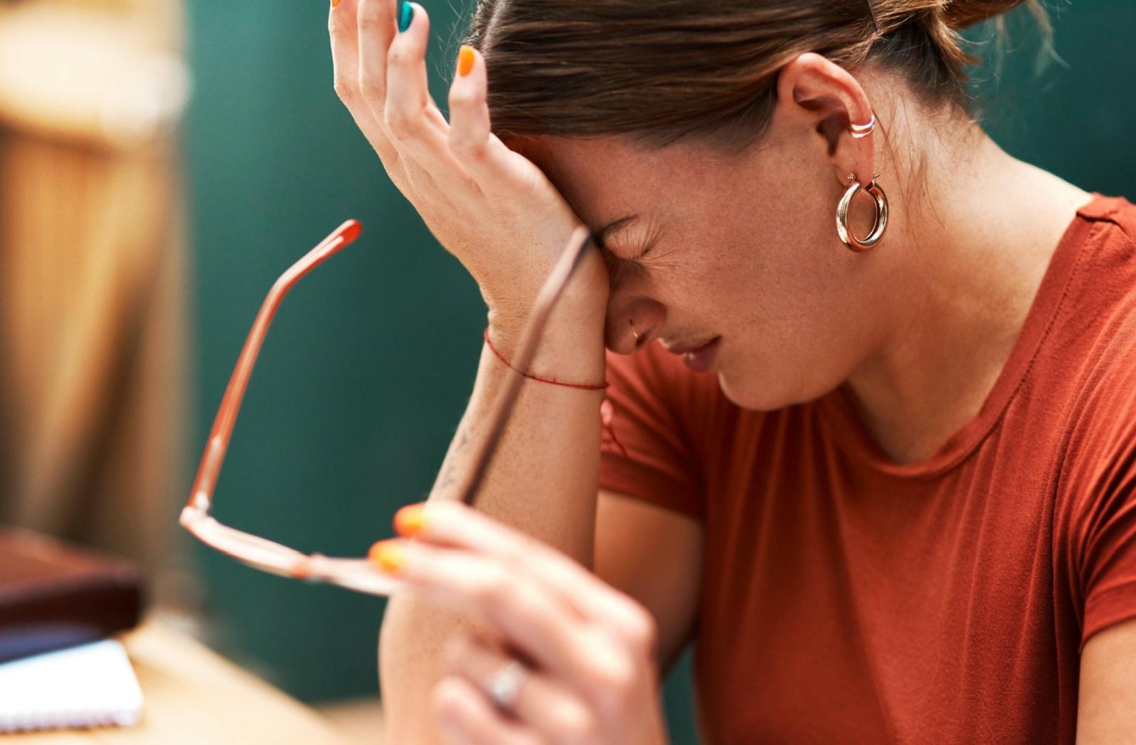 A person holding their glasses in one hand while they rub their forehead with their other hands